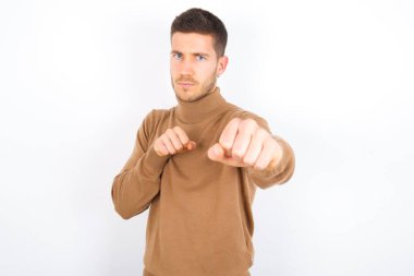 young caucasian man wearing turtleneck over white background Punching fist to fight, aggressive and angry attack, threat and violence