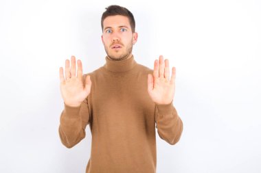 young caucasian man wearing turtleneck over white background Moving away hands palms showing refusal and denial with afraid and disgusting expression. Stop and forbidden.