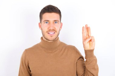 young caucasian man wearing turtleneck over white background showing and pointing up with fingers number three while smiling confident and happy.