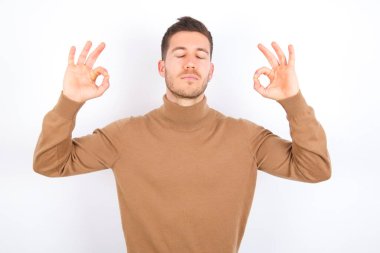 young caucasian man wearing turtleneck over white background relax and smiling with eyes closed doing meditation gesture with fingers. Yoga concept.