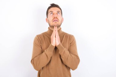 young caucasian man wearing turtleneck over white background begging and praying with hands together with hope expression on face very emotional and worried. Please God
