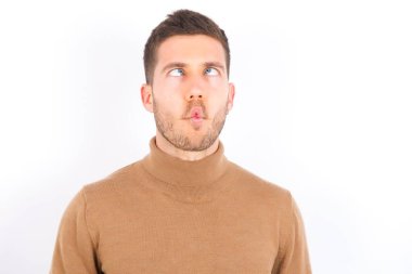 young caucasian man wearing turtleneck over white background making fish face with lips, crazy and comical gesture. Funny expression.