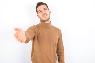 young caucasian man wearing turtleneck over white background smiling friendly offering handshake as greeting and welcoming. Successful business.