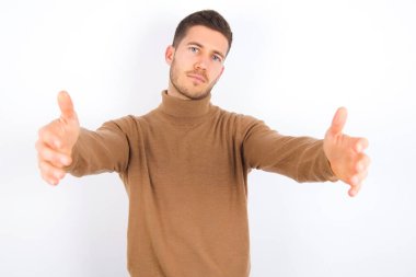 young caucasian man wearing turtleneck over white background looking at the camera smiling with open arms for hug. Cheerful expression embracing happiness.