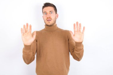 young caucasian man wearing turtleneck over white background afraid and terrified with fear expression stop gesture with hands, shouting in shock. Panic concept.