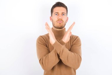 young caucasian man wearing turtleneck over white background Rejection expression crossing arms doing negative sign, angry face