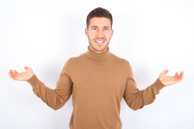 Cheerful cheery optimistic young caucasian man wearing turtleneck over white background holding two palms copy space