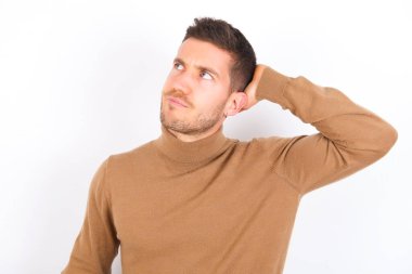 young caucasian man wearing turtleneck over white background confuse and wonder about question. Uncertain with doubt, thinking with hand on head. Pensive concept.