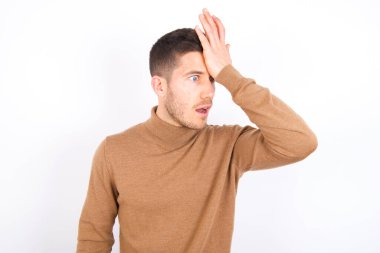 young caucasian man wearing turtleneck over white background surprised with hand on head for mistake, remember error. Forgot, bad memory concept.