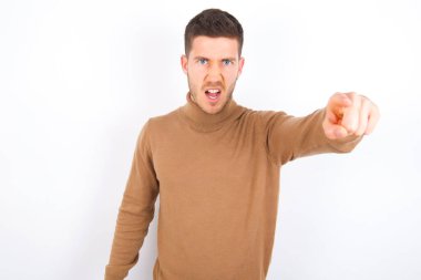 young caucasian man wearing turtleneck over white background pointing displeased and frustrated to the camera, angry and furious ready to fight with you.
