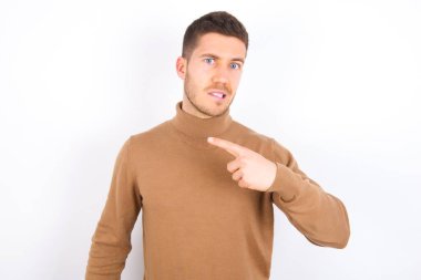 young caucasian man wearing turtleneck over white background Pointing aside worried and nervous with forefinger, concern and surprise concept.