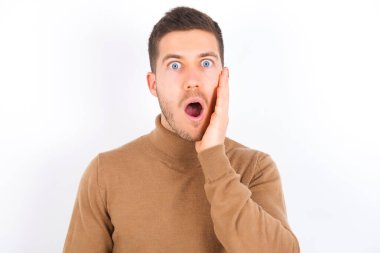 Shocked young caucasian man wearing turtleneck over white background looks with great surprisment being very stunned, astonished with unexpected news, Facial expressions concept.