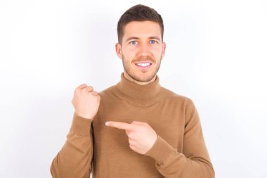 young caucasian man wearing turtleneck over white background In hurry pointing to wrist watch, impatience, looking at the camera with relaxed expression