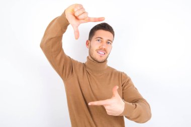 young caucasian man wearing turtleneck over white background making finger frame with hands. Creativity and photography concept.