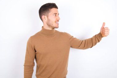 young caucasian man wearing turtleneck over white background Looking proud, smiling doing thumbs up gesture to the side. Good job!