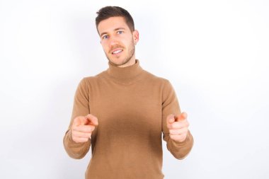 young caucasian man wearing turtleneck over white background pointing fingers to camera with happy and funny face. Good energy and vibes.