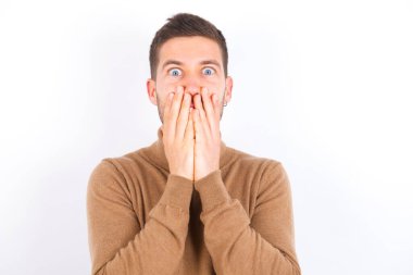 Vivacious young caucasian man wearing turtleneck over white background , giggles joyfully, covers mouth, has natural laughter, hears positive story or funny anecdote