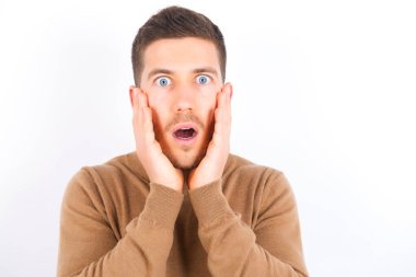 Scared terrified young caucasian man wearing turtleneck over white background shocked with prices at shop, People and human emotions concept