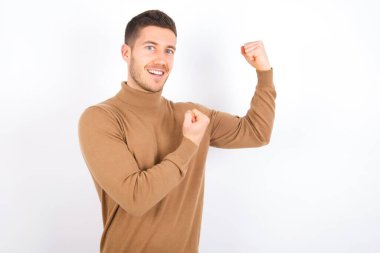 Profile photo of excited young caucasian man wearing turtleneck over white background raising fists celebrating black Friday shopping