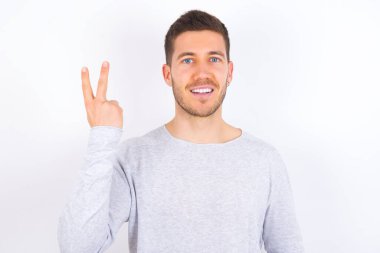 young caucasian man wearing casual clothes over white background smiling and looking friendly, showing number two or second with hand forward, counting down