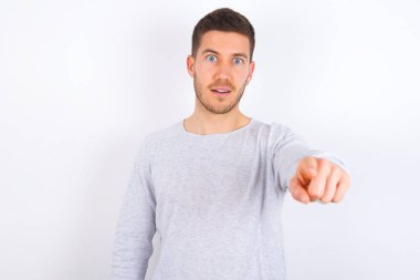 Excited positive young caucasian man wearing casual clothes over white background points index finger directly at you, sees something very funny. Wow, amazing