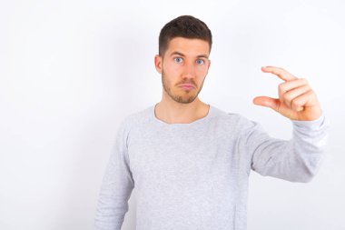 young caucasian man wearing casual clothes over white background purses lip and gestures with hand, shows something very little.