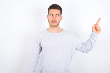 young caucasian man wearing casual clothes over white background points at copy space and advertises something, advices best price.