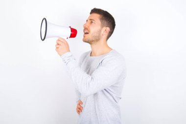 Funny young caucasian man wearing casual clothes over white background People sincere emotions lifestyle concept. Mock up copy space. Screaming in megaphone.