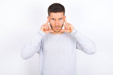 Serious concentrated young caucasian man wearing casual clothes over white background keeps fingers on temples, tries to ease tension, gather with thoughts and remember important information for exam