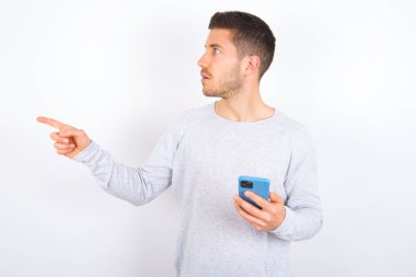 Stunned young caucasian man wearing casual clothes over white background points sideways right copy space, recommends product, sees astonishing thing