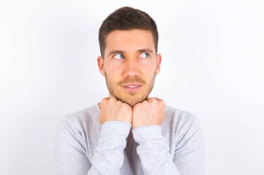 young caucasian man wearing casual clothes over white background holds hands under chin, glad to hear heartwarming words from stranger