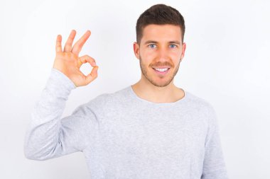 young caucasian man wearing casual clothes over white background hold hand arm okey symbol toothy approve advising novelty news
