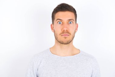 Stunned young caucasian man wearing casual clothes over white background stares reacts on shocking news. Astonished man holds breath