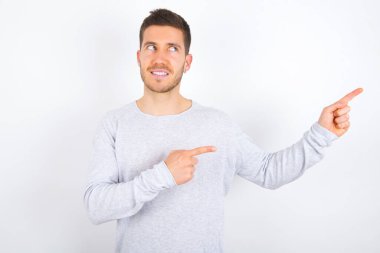 Optimistic young caucasian man wearing casual clothes over white background points with both hands and  looking at empty space.