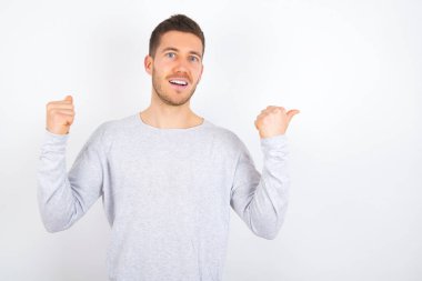 Hooray cool young caucasian man wearing casual clothes over white background point back empty space hand fist