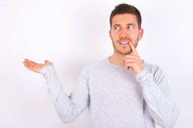 Positive young caucasian man wearing casual clothes over white background advert promo touch finger teeth