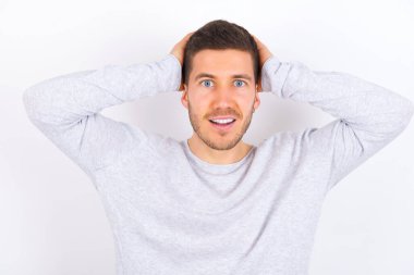 Cheerful overjoyed young caucasian man wearing casual clothes over white background reacts rising hands over head after receiving great news.