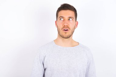 Shocked young caucasian man wearing casual clothes over white background look empty space with open mouth screaming: Oh My God! I can't believe this.