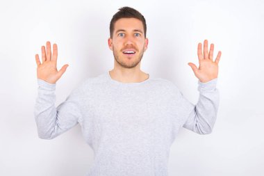 Delighted positive young caucasian man wearing casual clothes over white background opens mouth  and arms palms up after having great result
