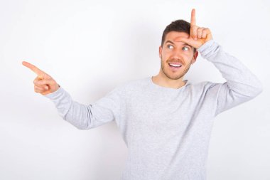 young caucasian man wearing casual clothes over white background showing loser sign and pointing at empty space