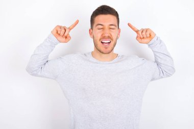 Photo of crazy young caucasian man wearing casual clothes over white background screaming and pointing with fingers at hair closed eyes