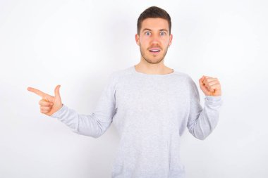 young caucasian man wearing casual clothes over white background points at empty space holding fist up, winner gesture.