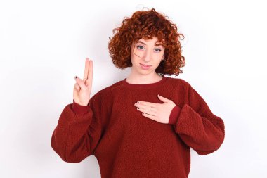 young caucasian woman red haired wearing red sweater over white background keeps smiling swearing with hand on chest and fingers up, making a loyalty promise oath.