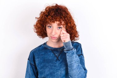 Disappointed dejected young caucasian woman red haired wearing blue T-shirt over white background wipes tears stands stressed with gloomy expression. Negative emotion