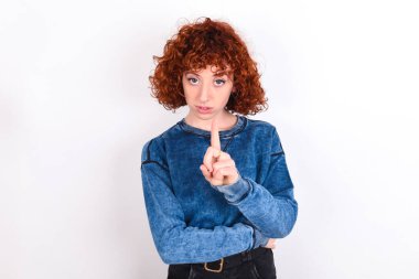young caucasian woman red haired wearing blue T-shirt over white background frustrated and pointing to the front