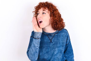 young caucasian woman red haired wearing blue T-shirt over white background look empty space holding hand near her face and screaming or calling someone.