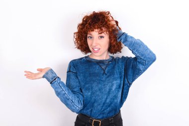 Shocked amazed surprised young caucasian woman red haired wearing blue T-shirt over white background hold hand offering proposition