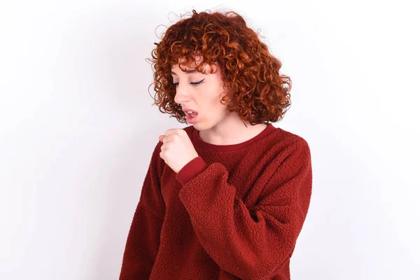 young caucasian woman red haired wearing red sweater over white background keeps feeling unwell and coughing as symptom for cold or bronchitis. Healthcare concept.