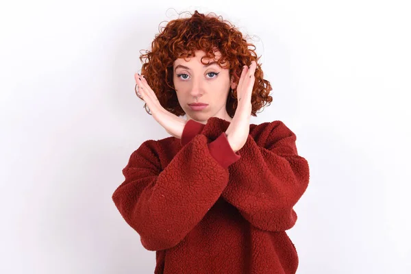 young caucasian woman red haired wearing red sweater over white background keeps Rejection expression crossing arms doing negative sign, angry face
