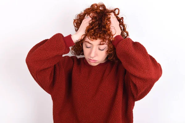 young caucasian woman red haired wearing red sweater over white background keeps suffering from strong headache desperate and stressed because of overwork. Depression and pain concept.